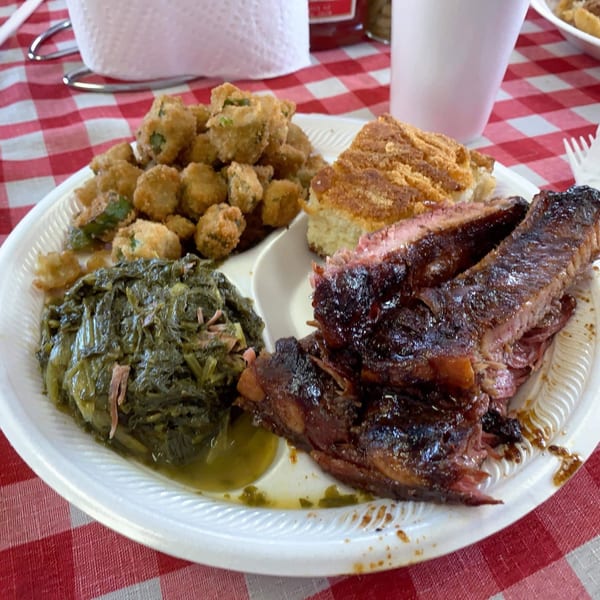 Scruggs BBQ plate with ribs, fried okra, cornbread, and collard greens on a red checkered tablecloth.
