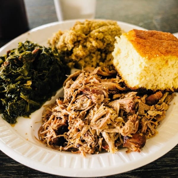 A Scruggs BBQ plate with pulled pork, collard greens, cornbread, and a side of mac and cheese.