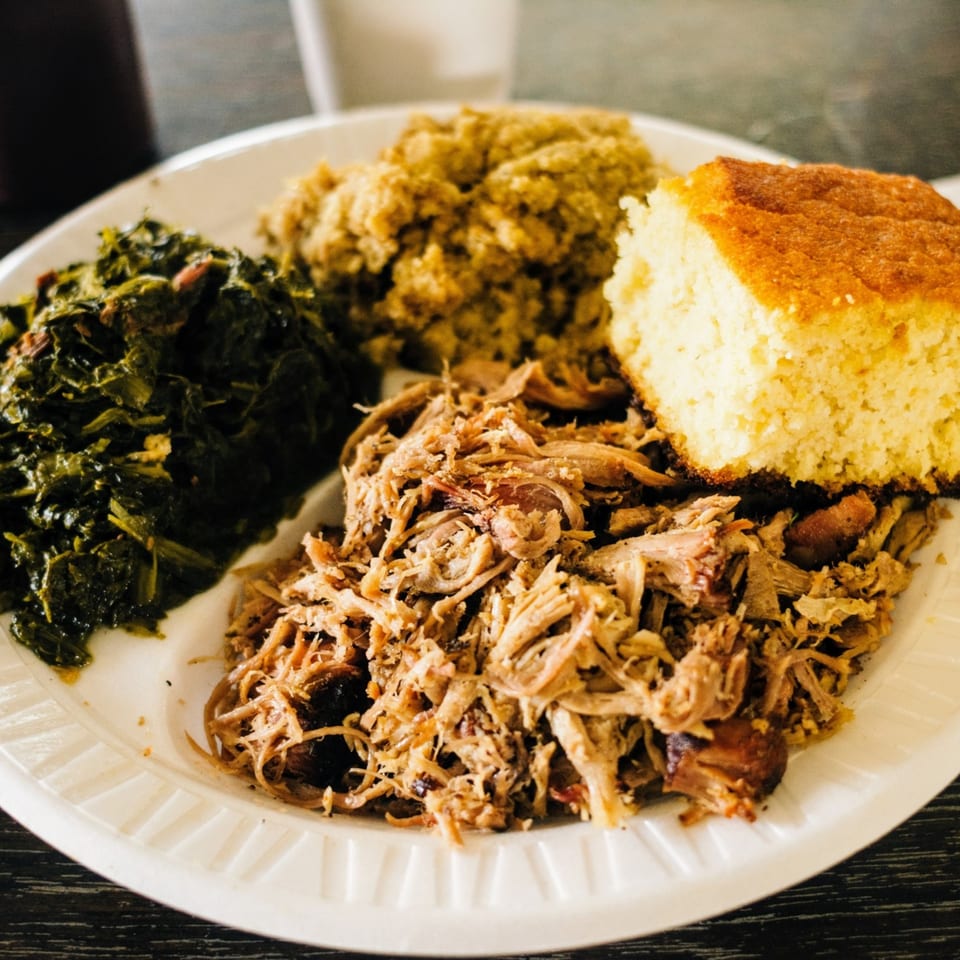 A Scruggs BBQ plate with pulled pork, collard greens, cornbread, and a side of mac and cheese.