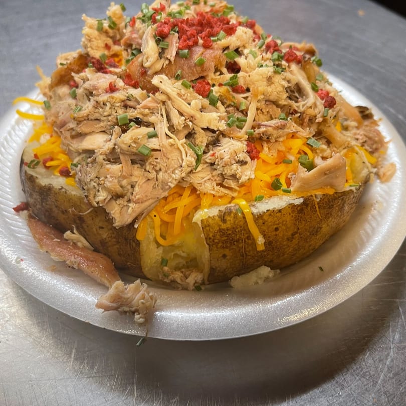 A Scruggs BBQ baked potato overflowing with shredded chicken, cheese, chives, and red sprinkles.